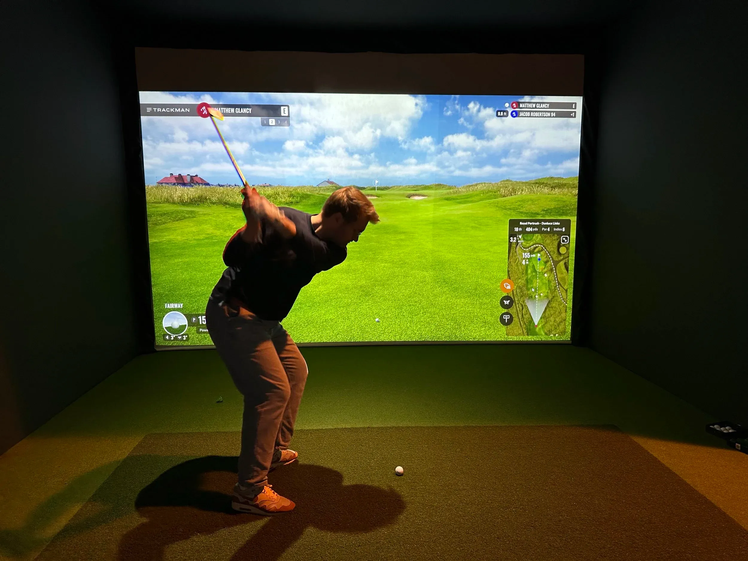 Golfer mid-swing in a Trackman simulator bay